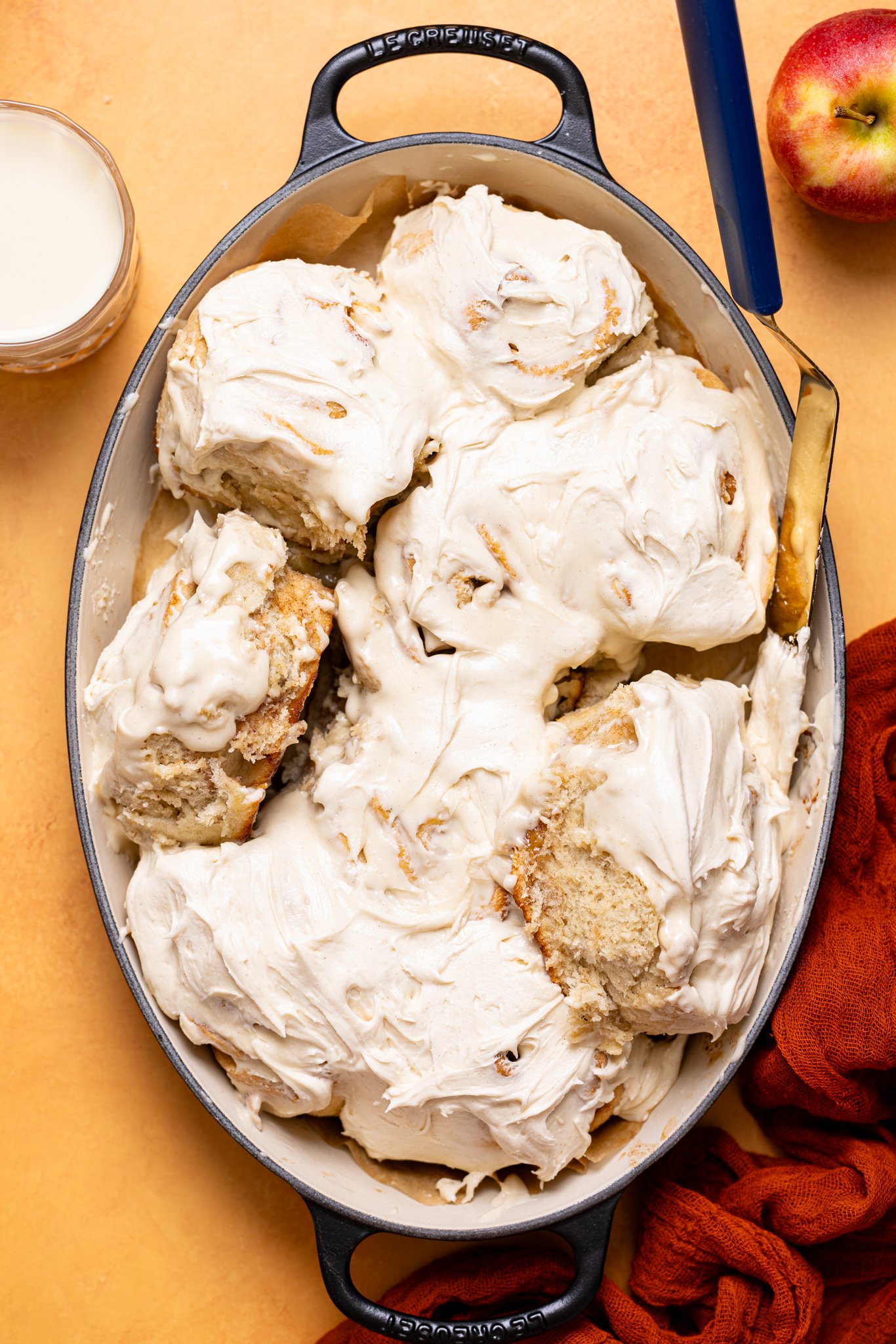 Frosted cinnamon rolls in a baking dish with a side of milk and an apple.