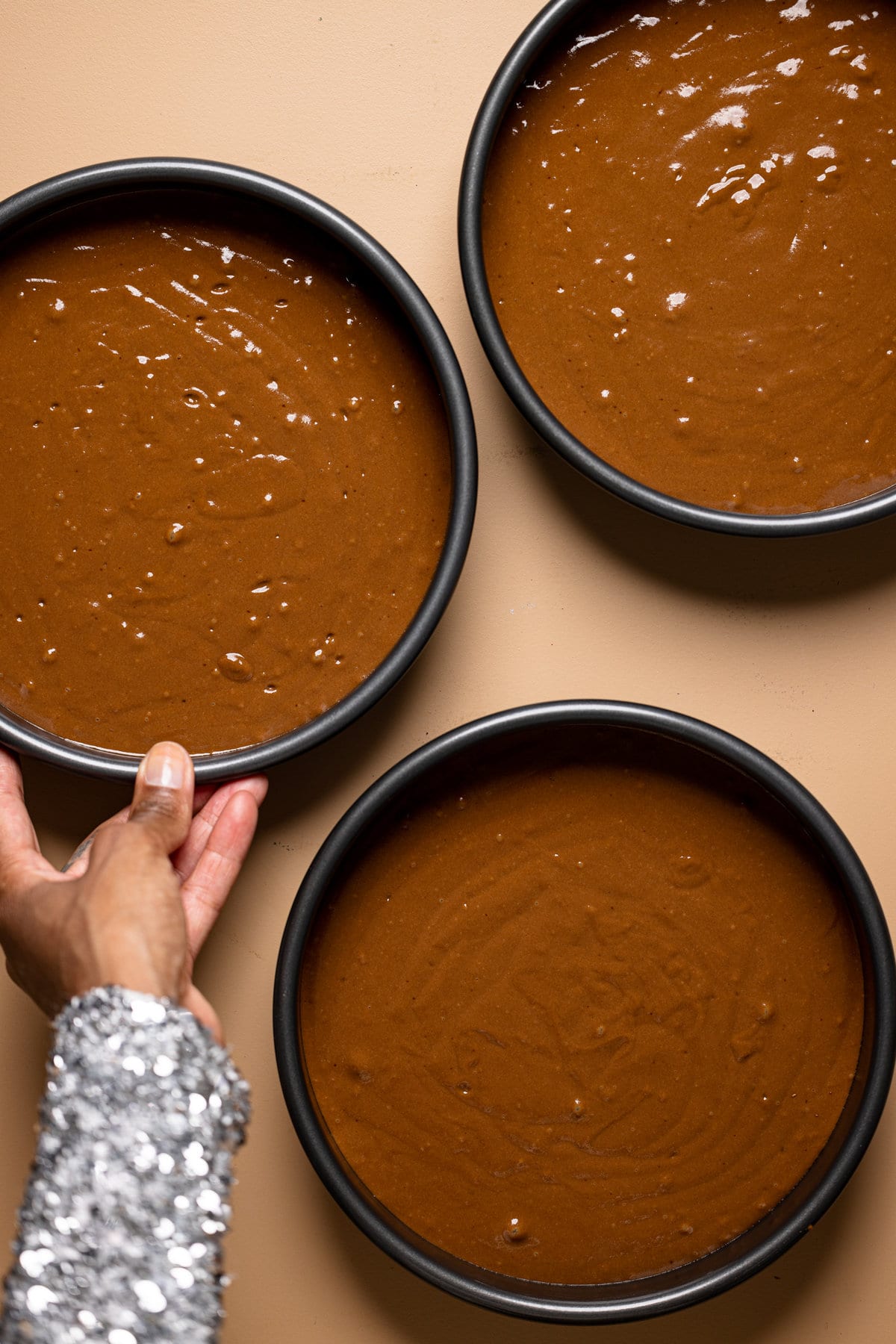 Three round pans filled with vegan chocolate cake batter