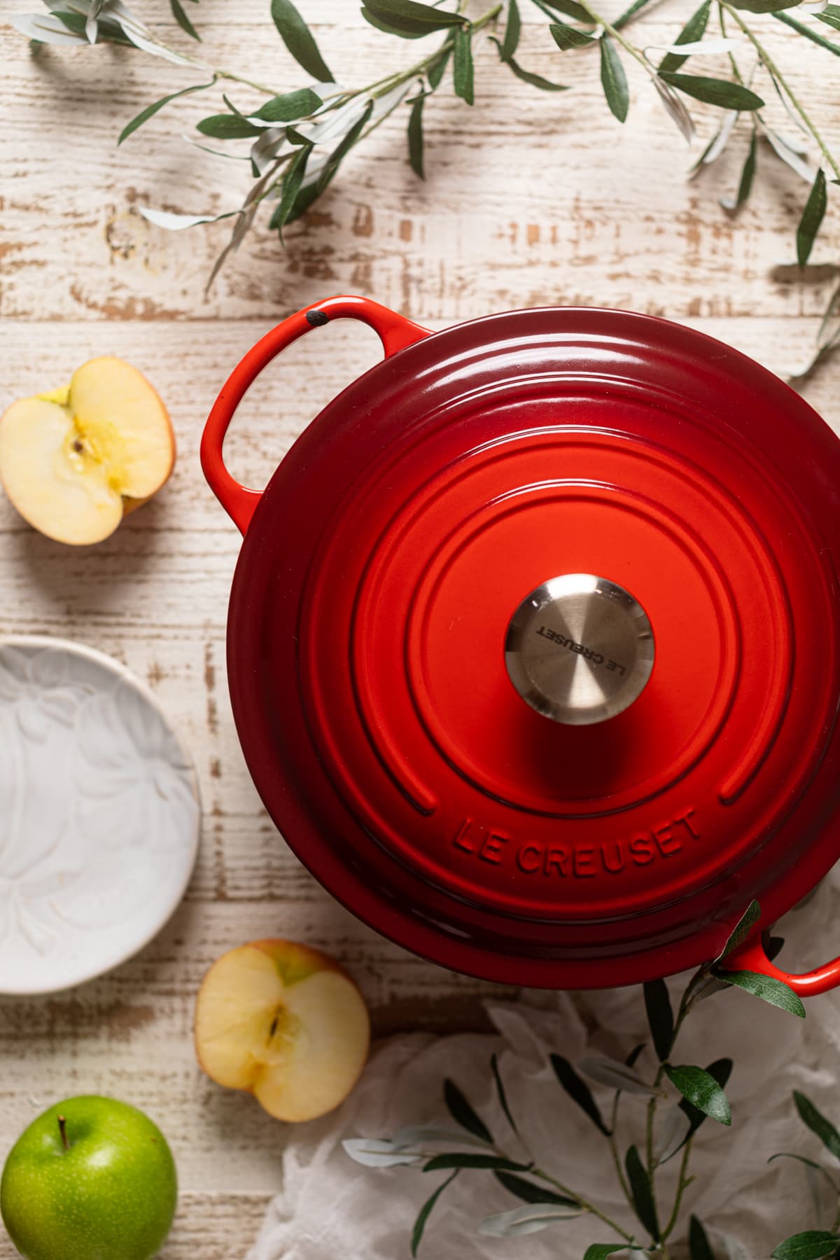 Red Le Creuset Dutch oven on a table with apples