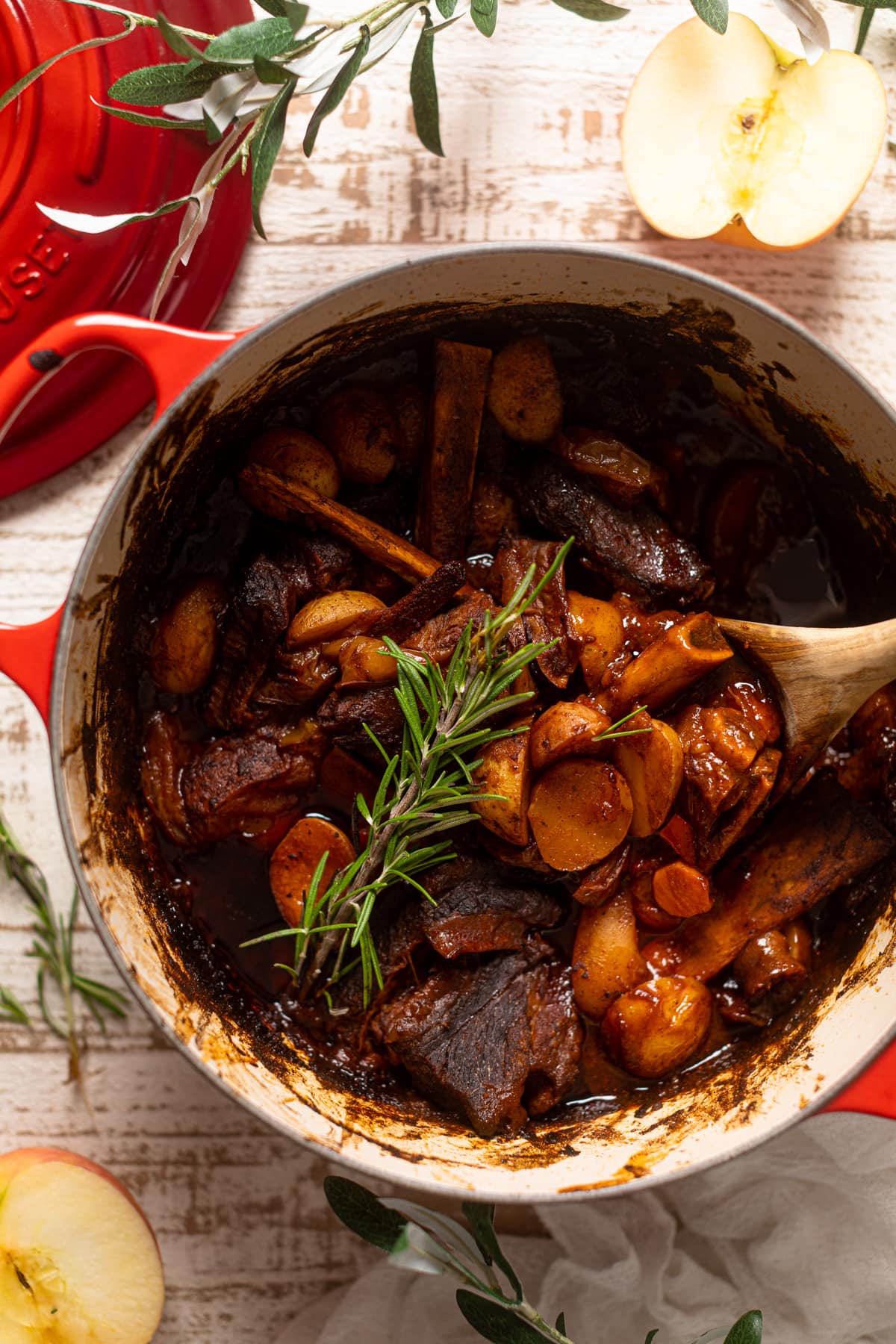 Wooden spoon stirring a pan of Slow cooked Braised Apple barbeque meat with Potatoes