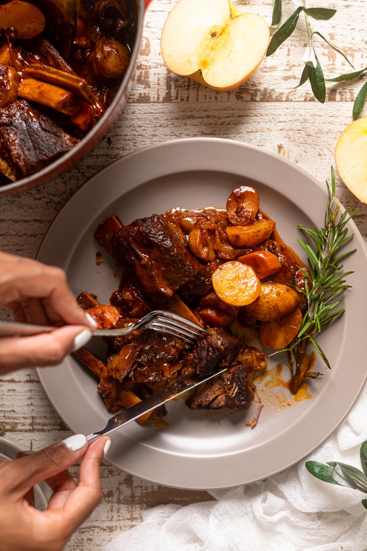 Hands using silverware to cut up Ribs with Potatoes