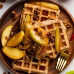 Pile of Apple Spice Cornmeal Waffles topped with caramelized apples and granola