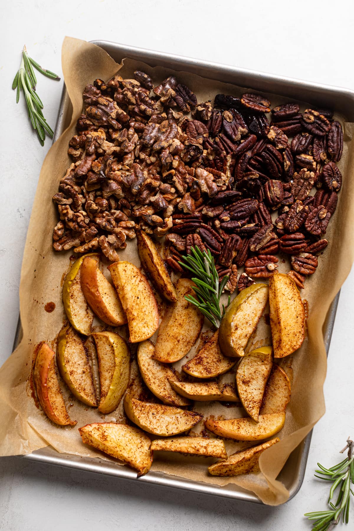 Seasoned nuts and apple slices on a baking sheet