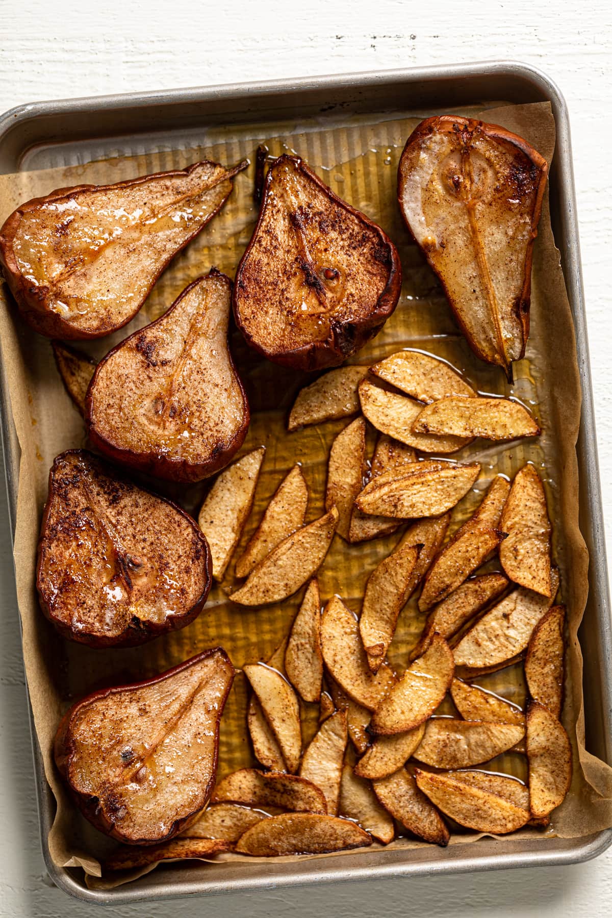 Roasted apple slices and halved pears on a baking sheet