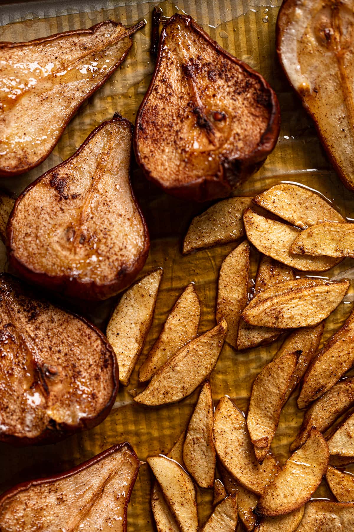 Roasted apple slices and halved pears on a baking sheet