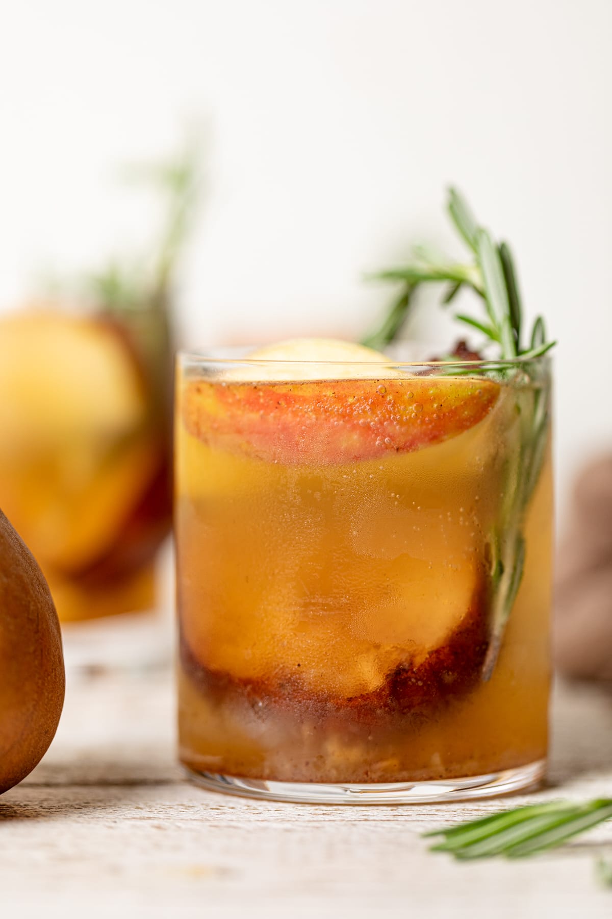 Roasted Apple Pear Mocktail in a small glass stuffed with apple slices and a sprig of rosemary
