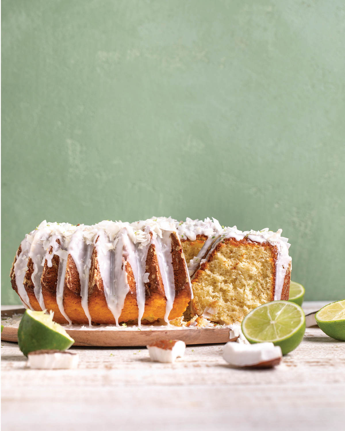 Partially sliced cake on a wooden board with lime halves and coconut pieces