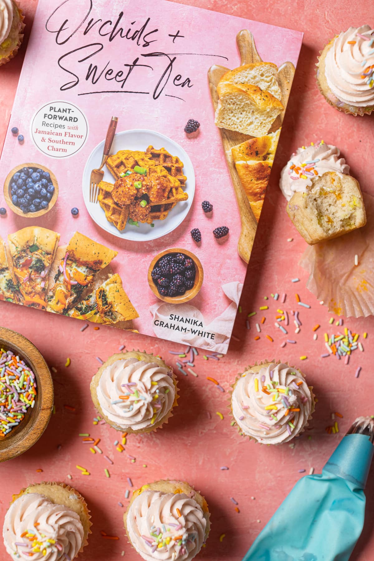 Orchids + Sweet Tea cookbook, cupcakes, and sprinkles on a pink table