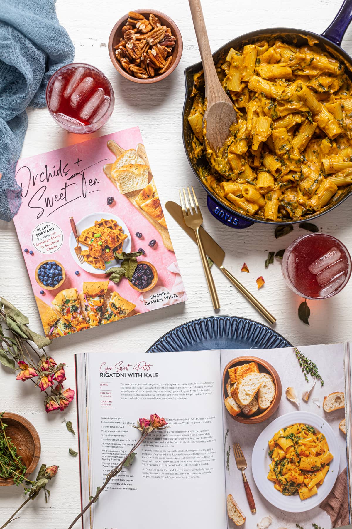 Orchid + Sweet Tea cookbooks on a table with plates, glasses, and a skillet of pasta