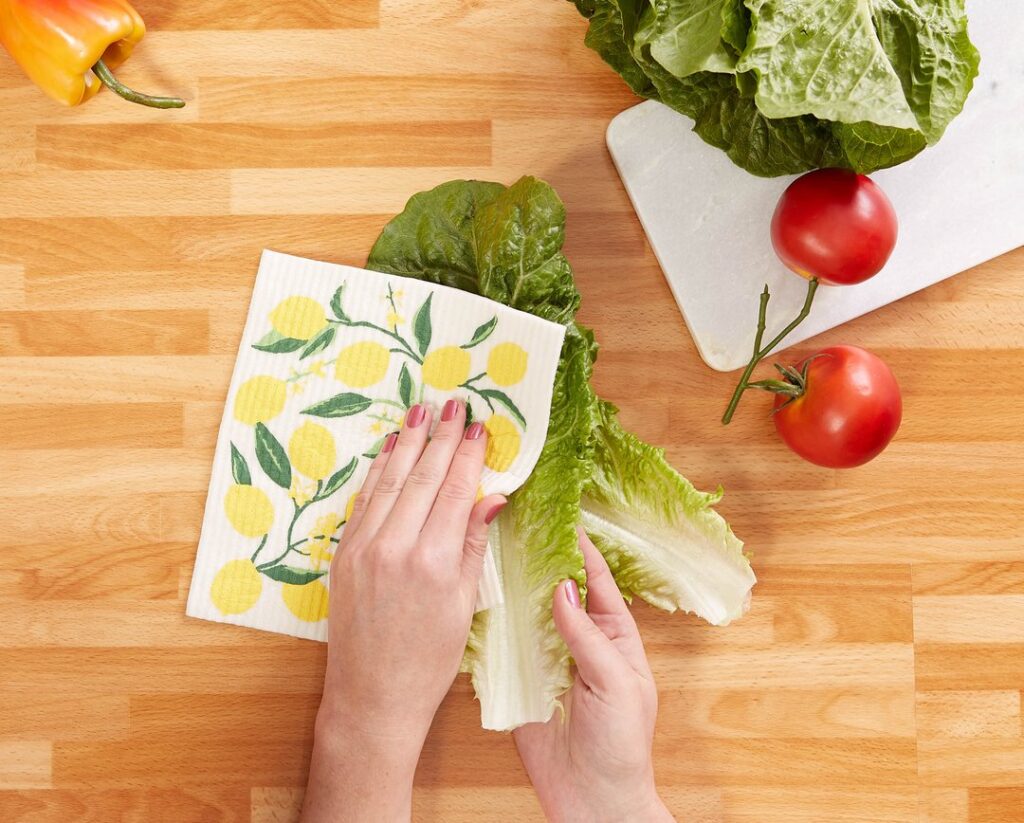 Hands using a Swedish dishcloth with a lemon design to wipe lettuce