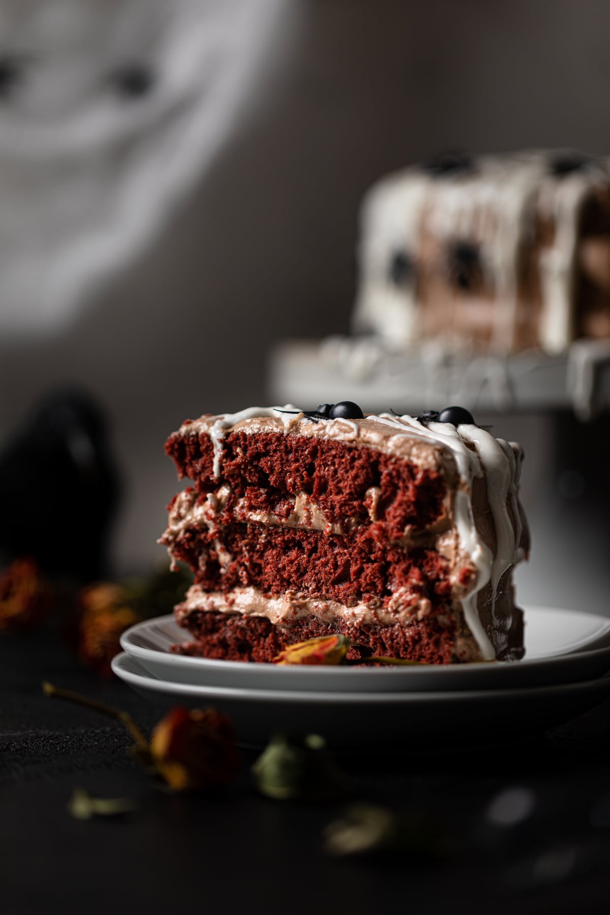 Slice of Black Widow Red Velvet Cake topped with spiders on two small stacked plates