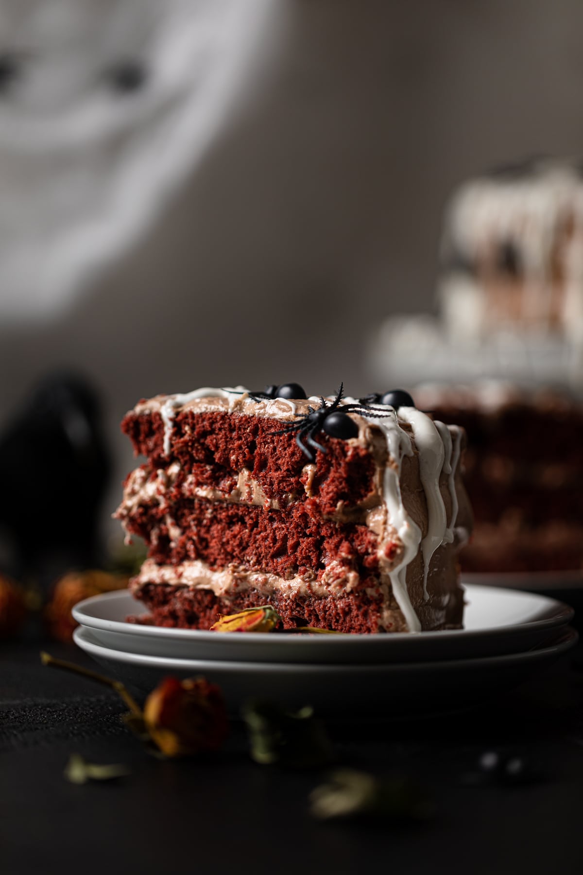 Slice of Black Widow Red Velvet Cake topped with spiders on two small, stacked plates