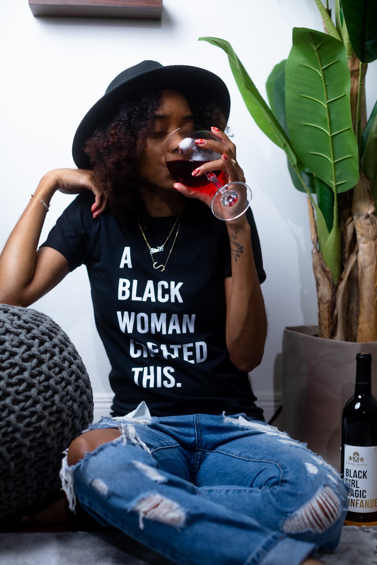 Shanika drinking Black Girl Magic wine while wearing a shirt that says \"A Black Woman Created This\"