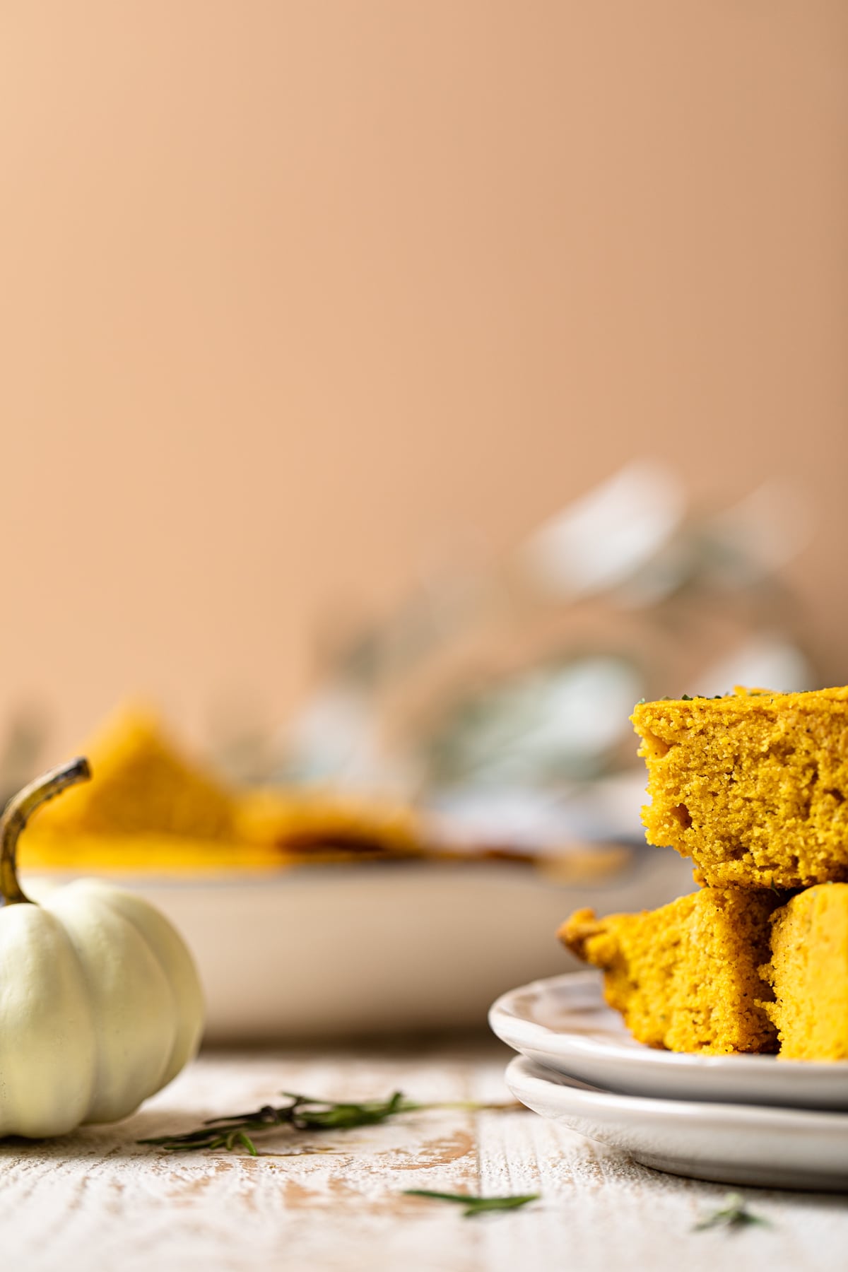 Pieces of Brown Butter Pumpkin Cornbread on small plates next to a small, white pumpkin