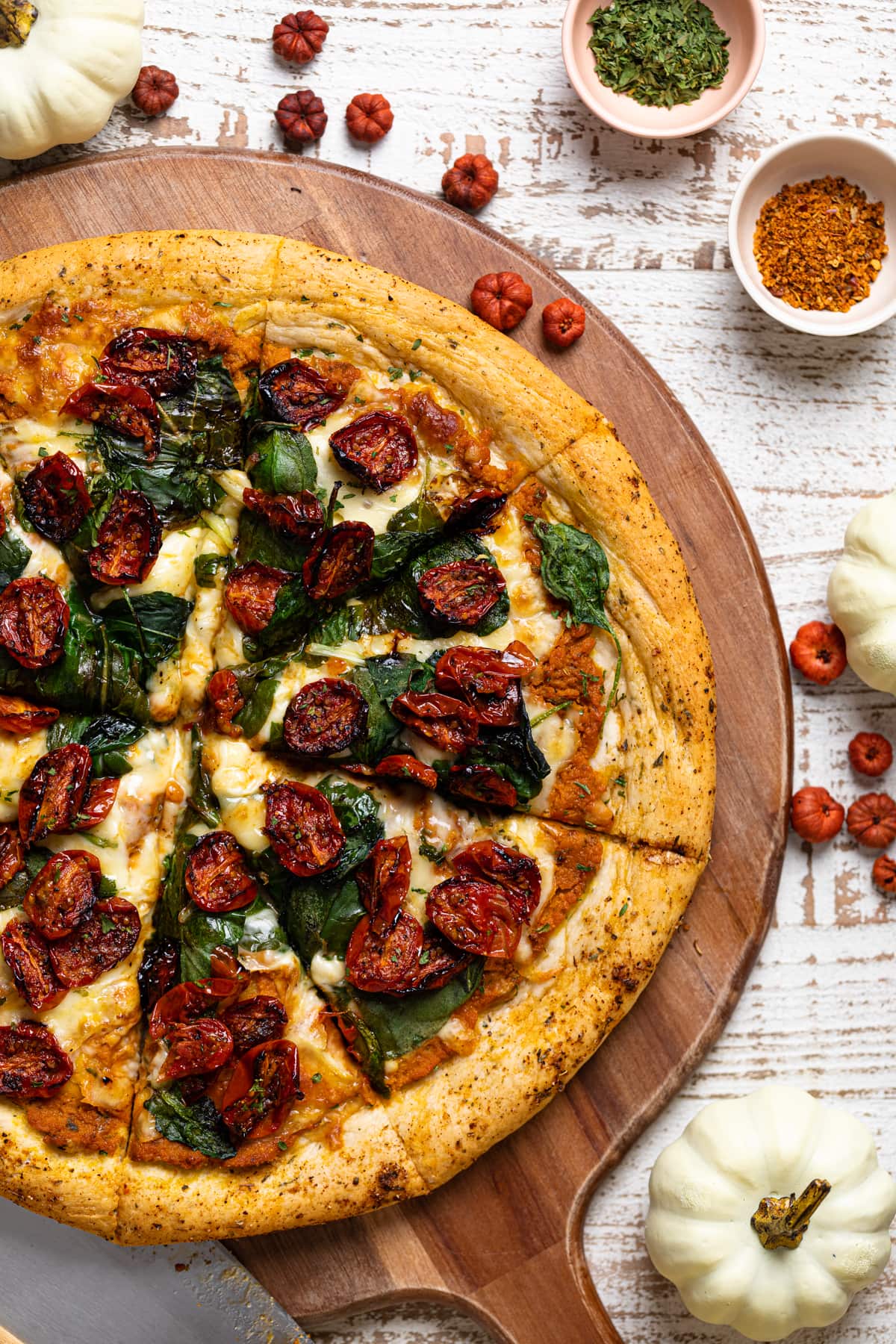 Partially-sliced Cajun Roasted Veggie Pumpkin Pizza on a wooden board