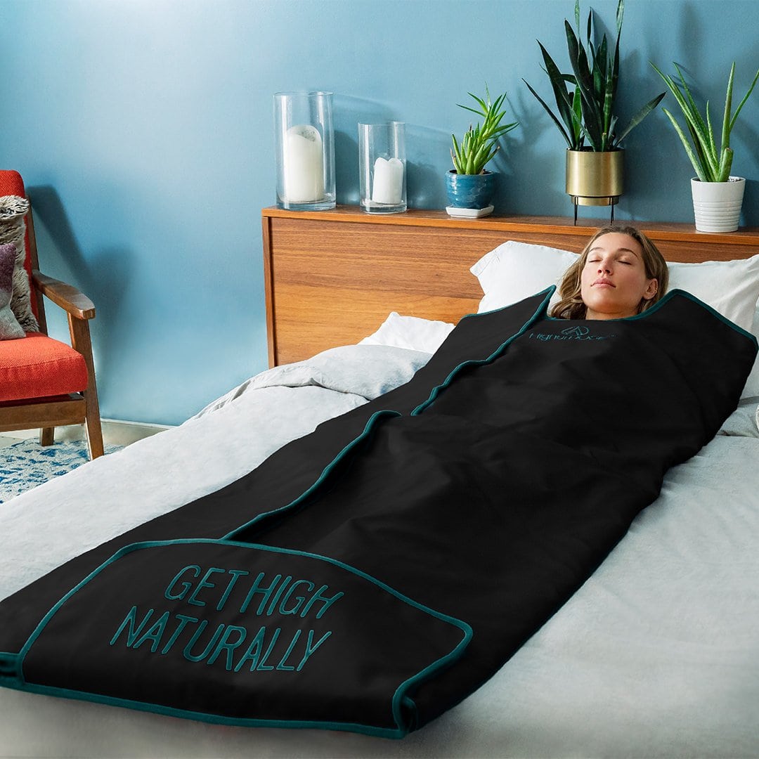 Woman on a bed inside an infrared sauna blanket that reads \"Get High Naturally\"