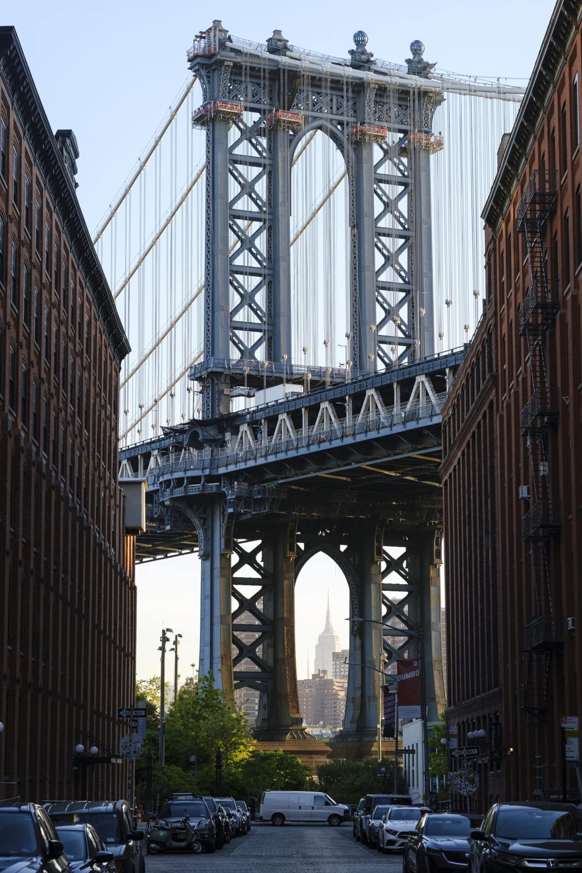 Bridge as seen between two buildings on either side of a street full of parked cars