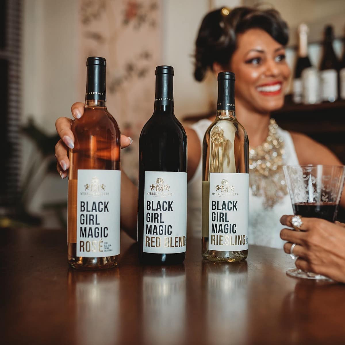 Woman smiling behind three bottles of Black Girl Magic wine