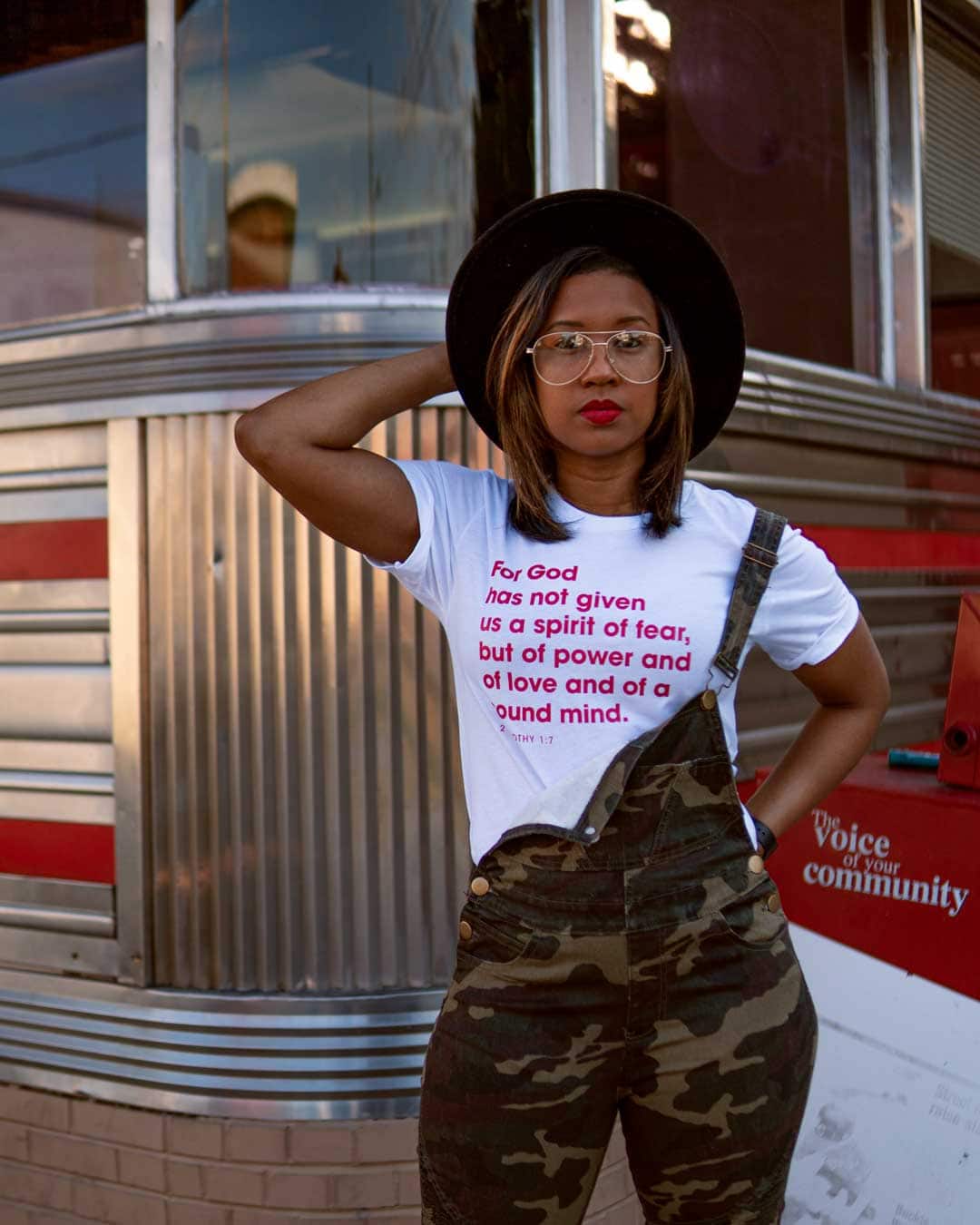 Woman with camo overalls and a shirt that reads: \"For God has not given us a spirit of fear, but of power and of love and of a sound mind.\"