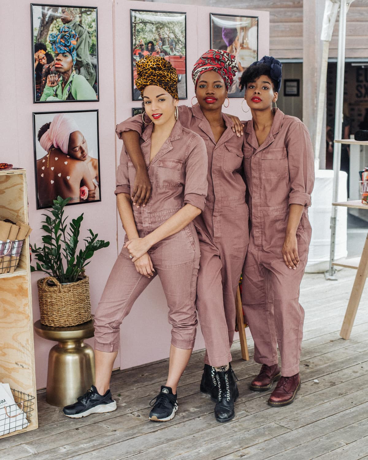 Three women in pink coveralls wearing different-colored head wraps