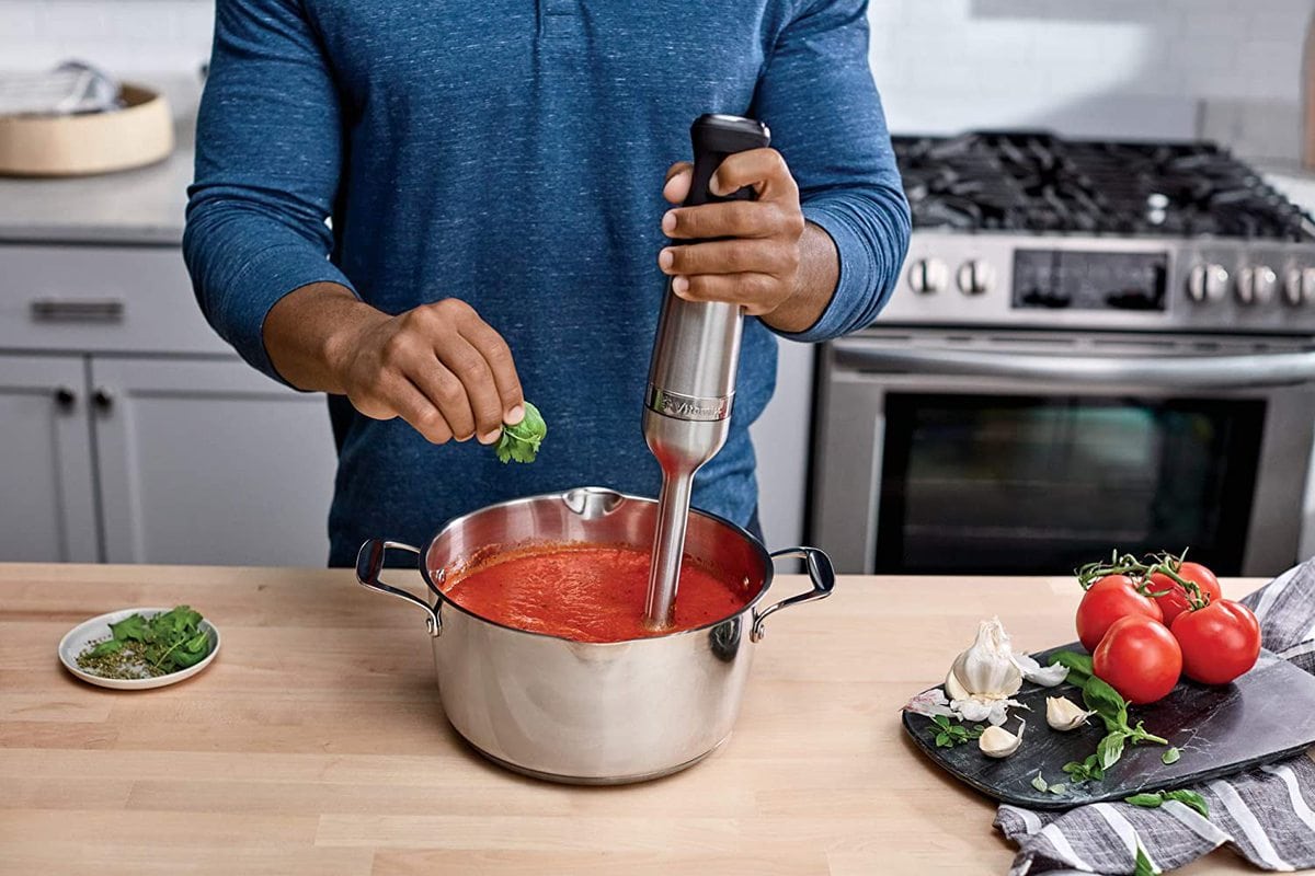 Man using a Vitamix immersion blender in a pan of red sauce