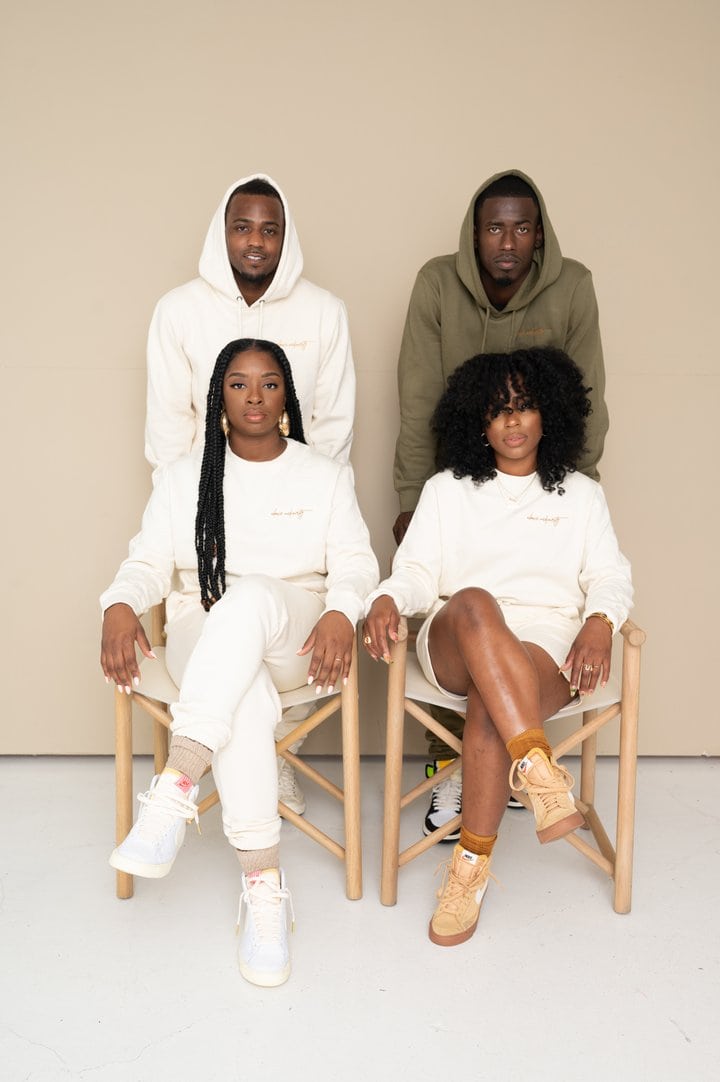 Two black women wearing light clothing sitting in chairs in front of two black men wearing hoodies - one light, one green