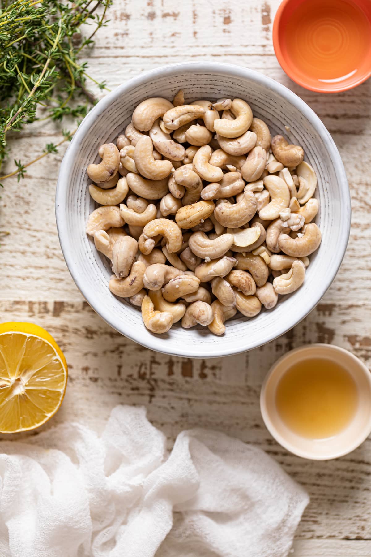 Bowl of cashews next to a lemon half, thyme leaves, and other ingredients