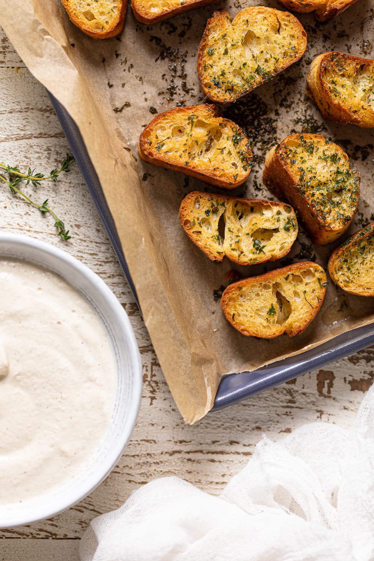 Seasoned, toasted bread slices on a baking sheet next to a bowl of vegan cream cheese sauce