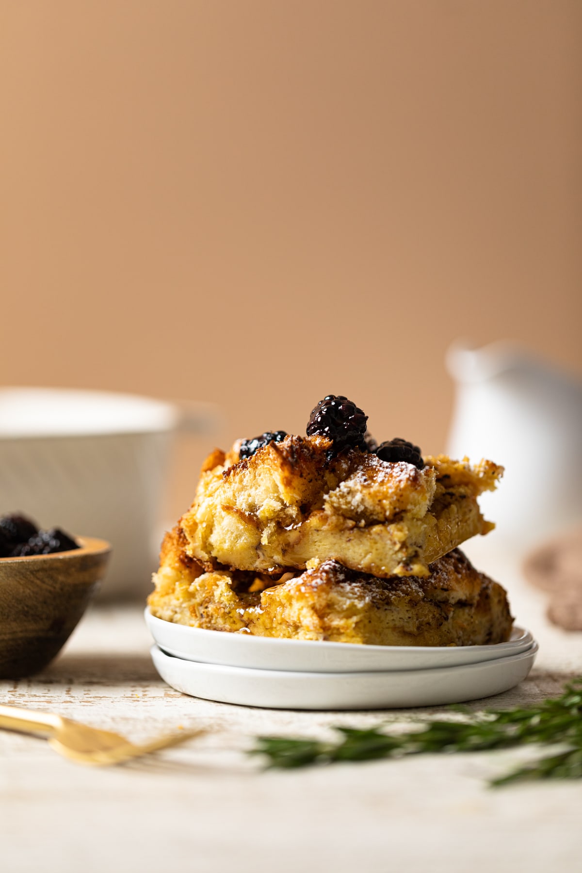 Pieces of Cinnamon Brown Butter French Toast Casserole on two small, stacked plates topped with blackberries