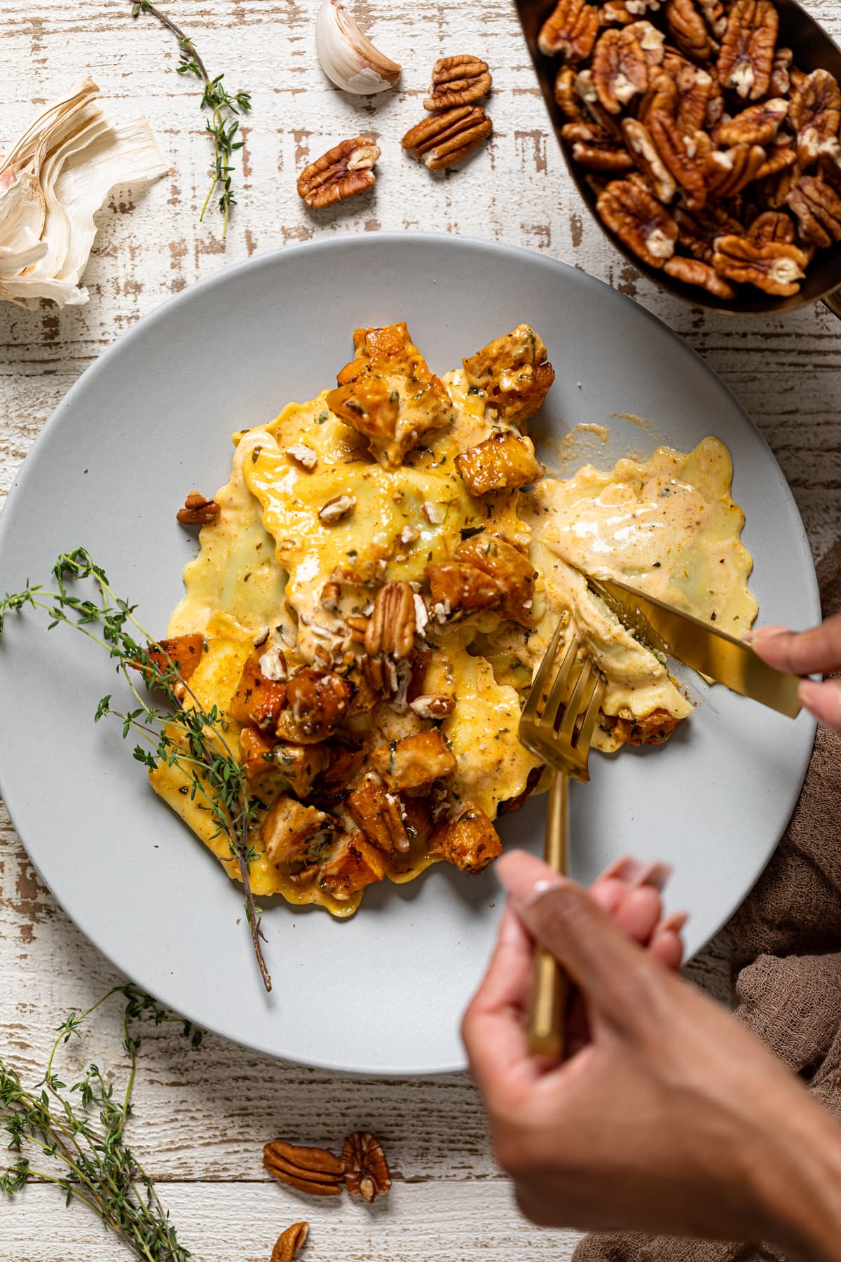 Hands using silverware to cut Ravioli with Parmesan Garlic Sauce