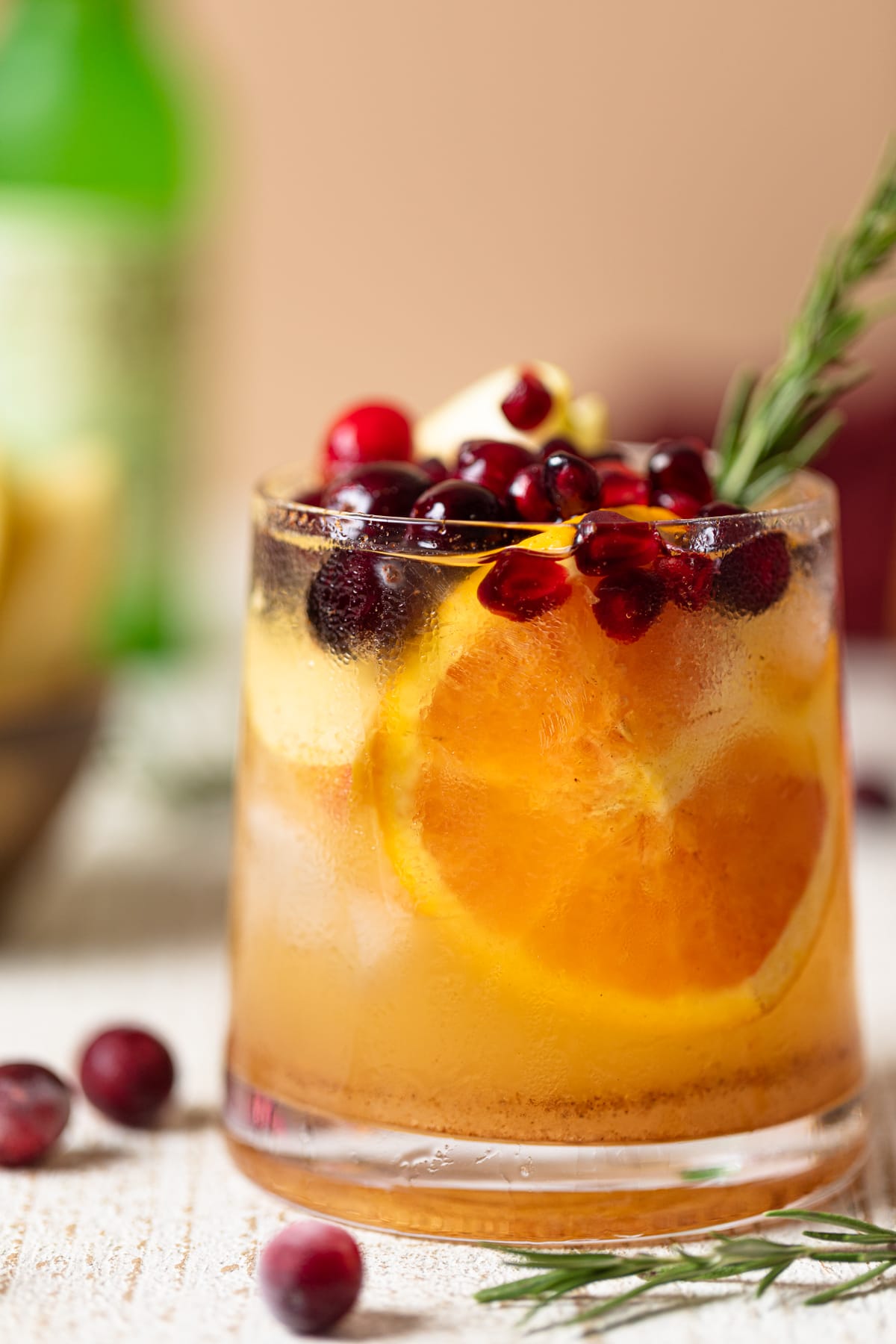 Closeup of a Thanksgiving Punch Mocktail topped with pomegranate arils, cranberries, and a rosemary sprig