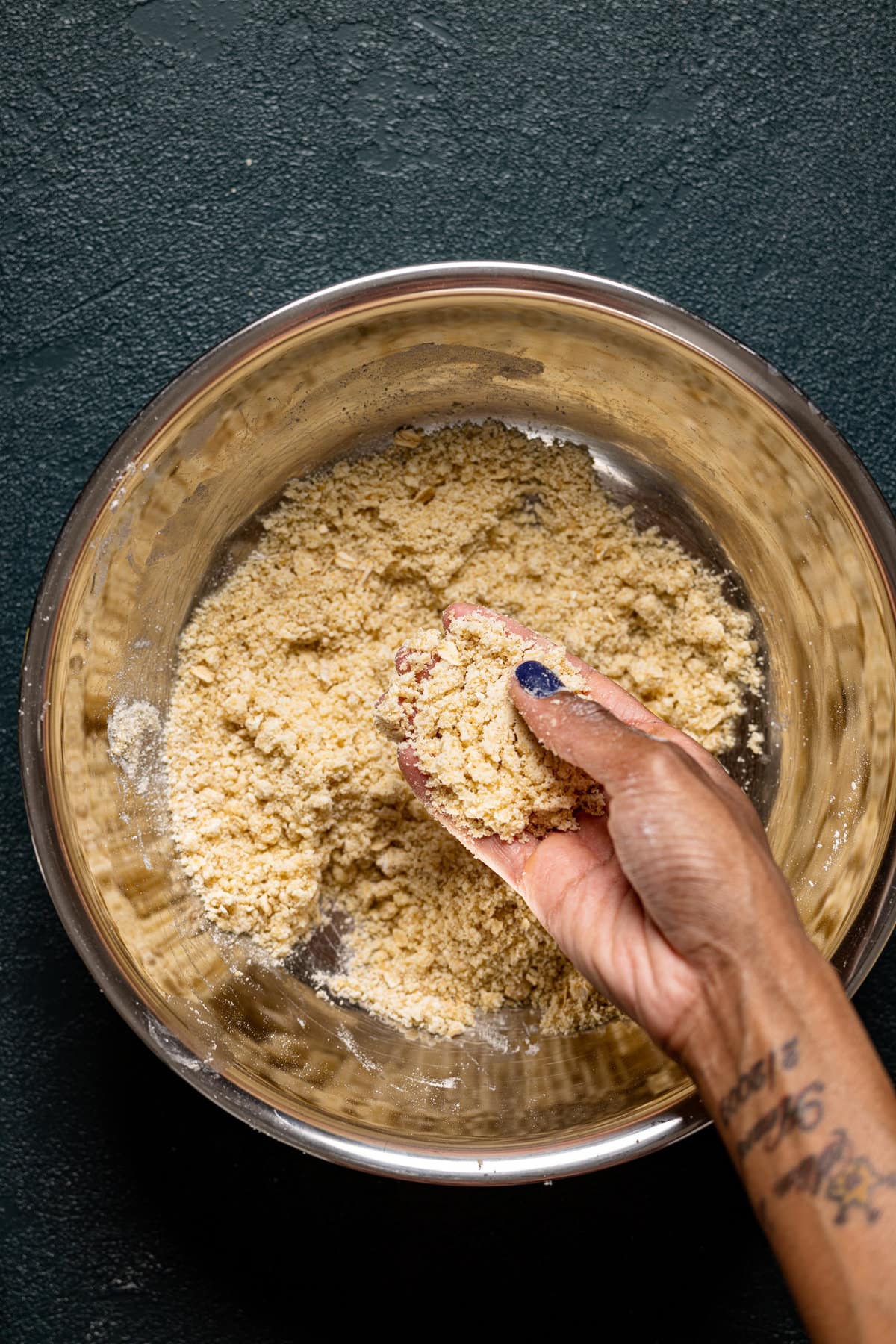 Hand holding some crumb topping over a bowl full of crumb topping