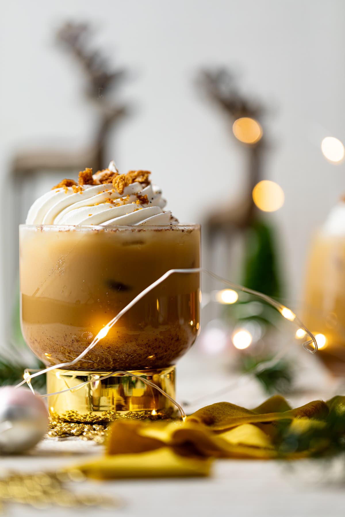 Gingerbread Eggnog Mocktail in a gold-stemmed glass surrounded by small Christmas lights