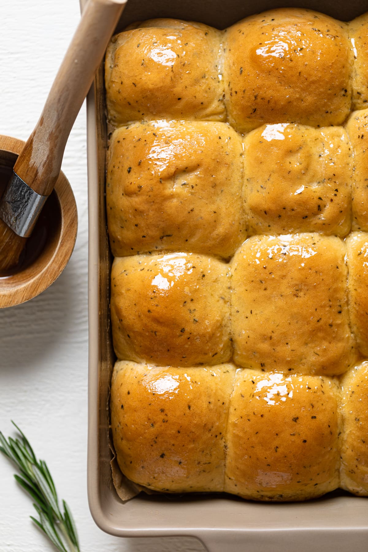 Baking dish of Honey Herb Dinner Rolls next to a small wooden bowl of honey butter