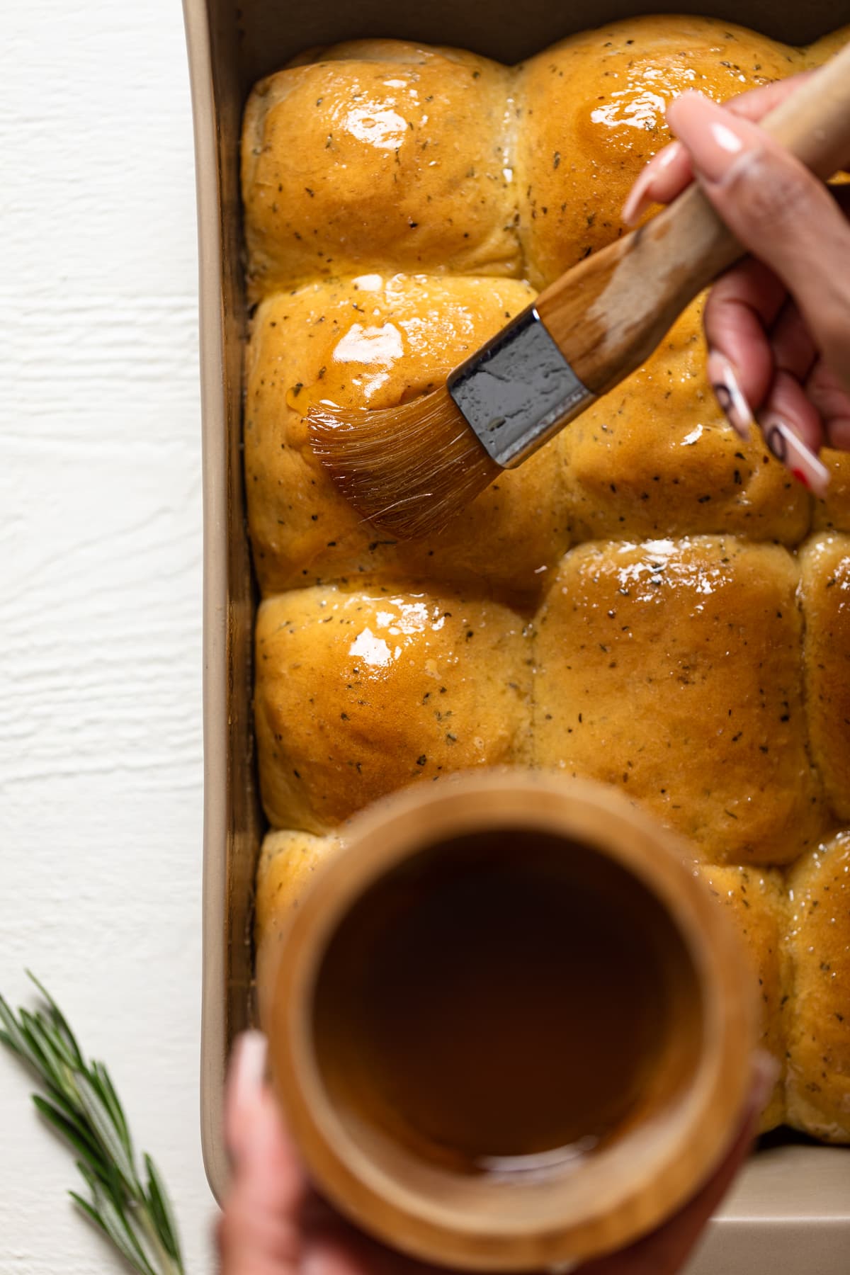 Brush painting honey butter onto Hot Honey Herb Dinner Rolls