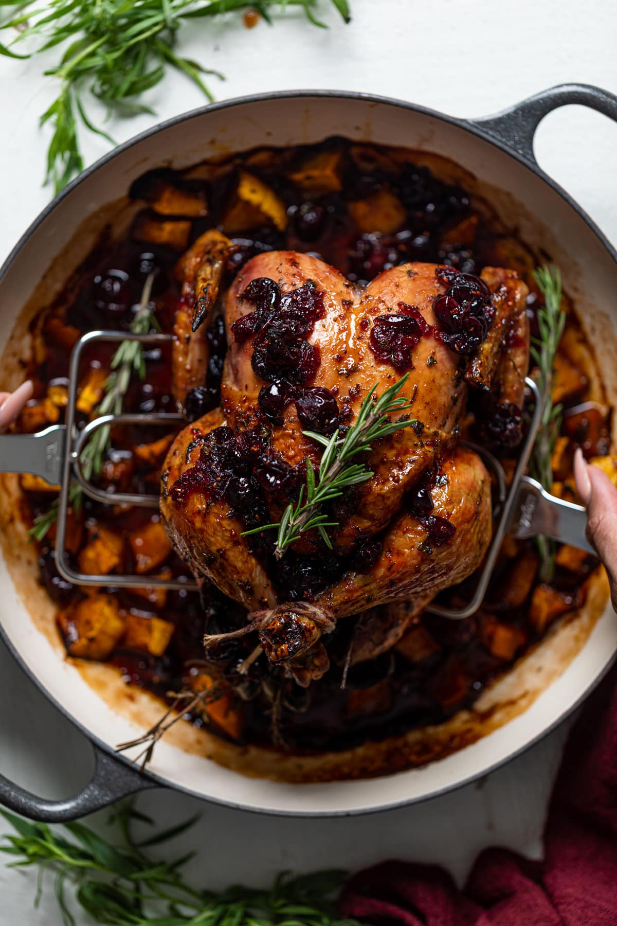 Serving utensils lifting a Cranberry Maple Roast Chicken out of a Dutch oven