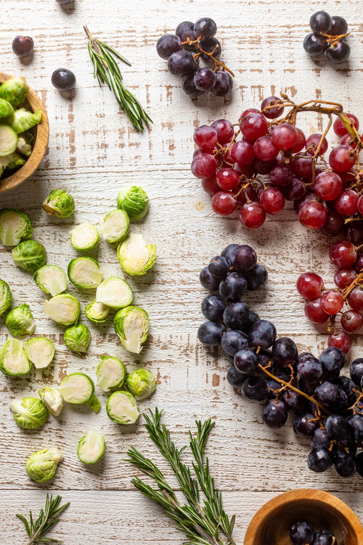 Grapes, brussels sprouts, and rosemary sprigs on a white table