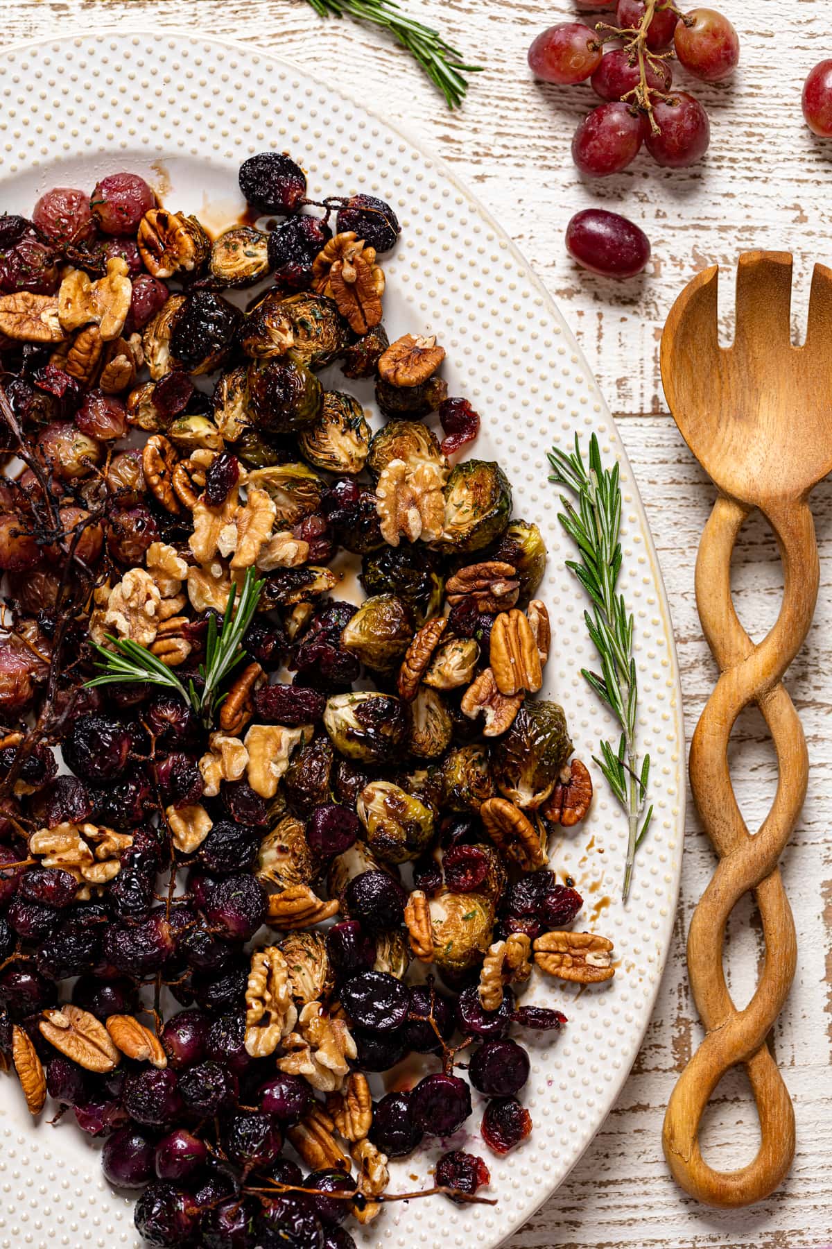 Roasted Grapes and Brussels Sprouts on a white serving platter with a wooden serving spoon with a twisted handle