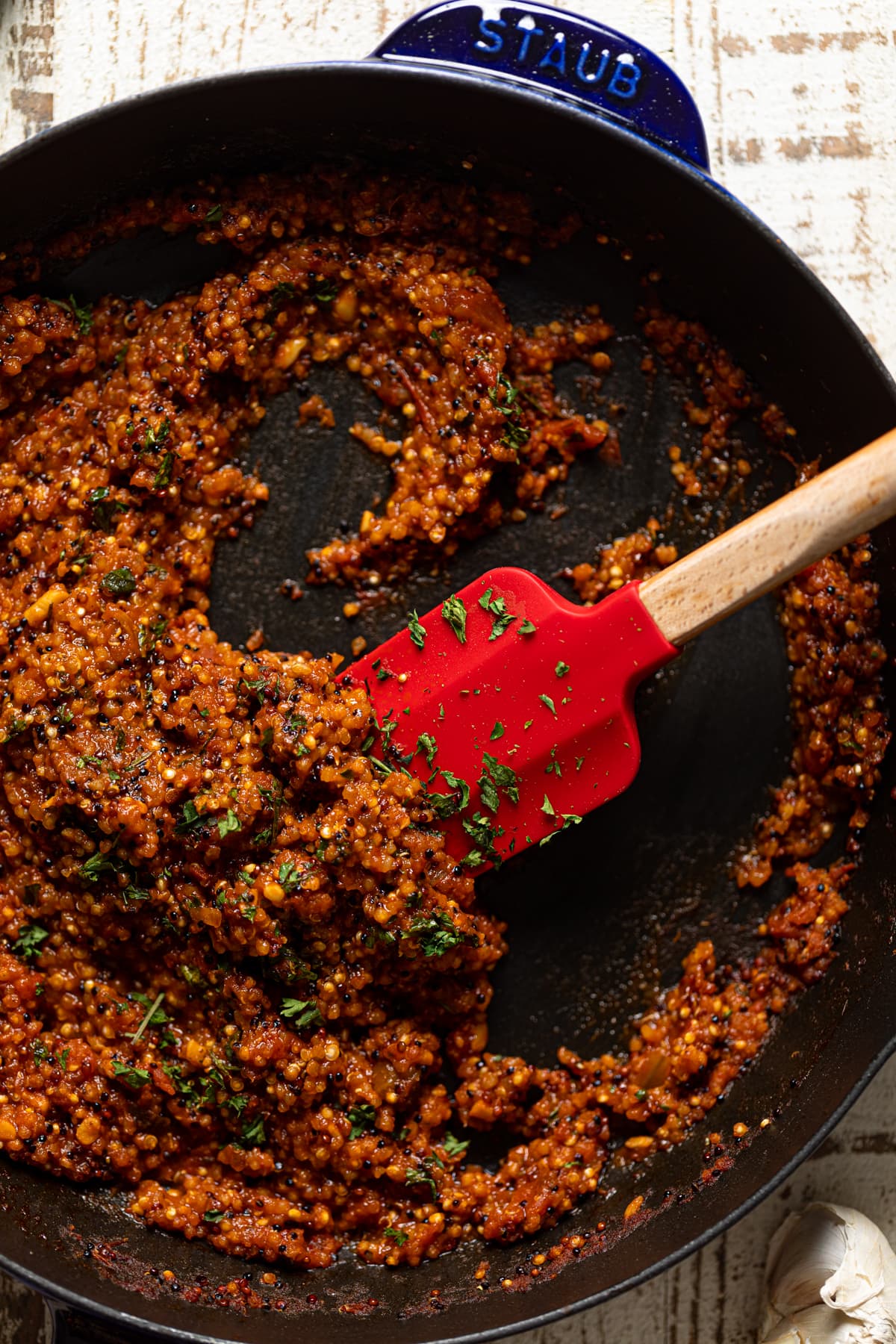 Red spatula in a skillet of seasoned quinoa
