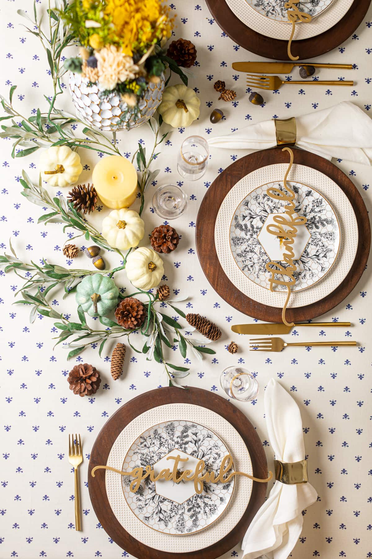 Decorative place settings, pumpkins, candles, and pine cones on a mostly-white tablecloth