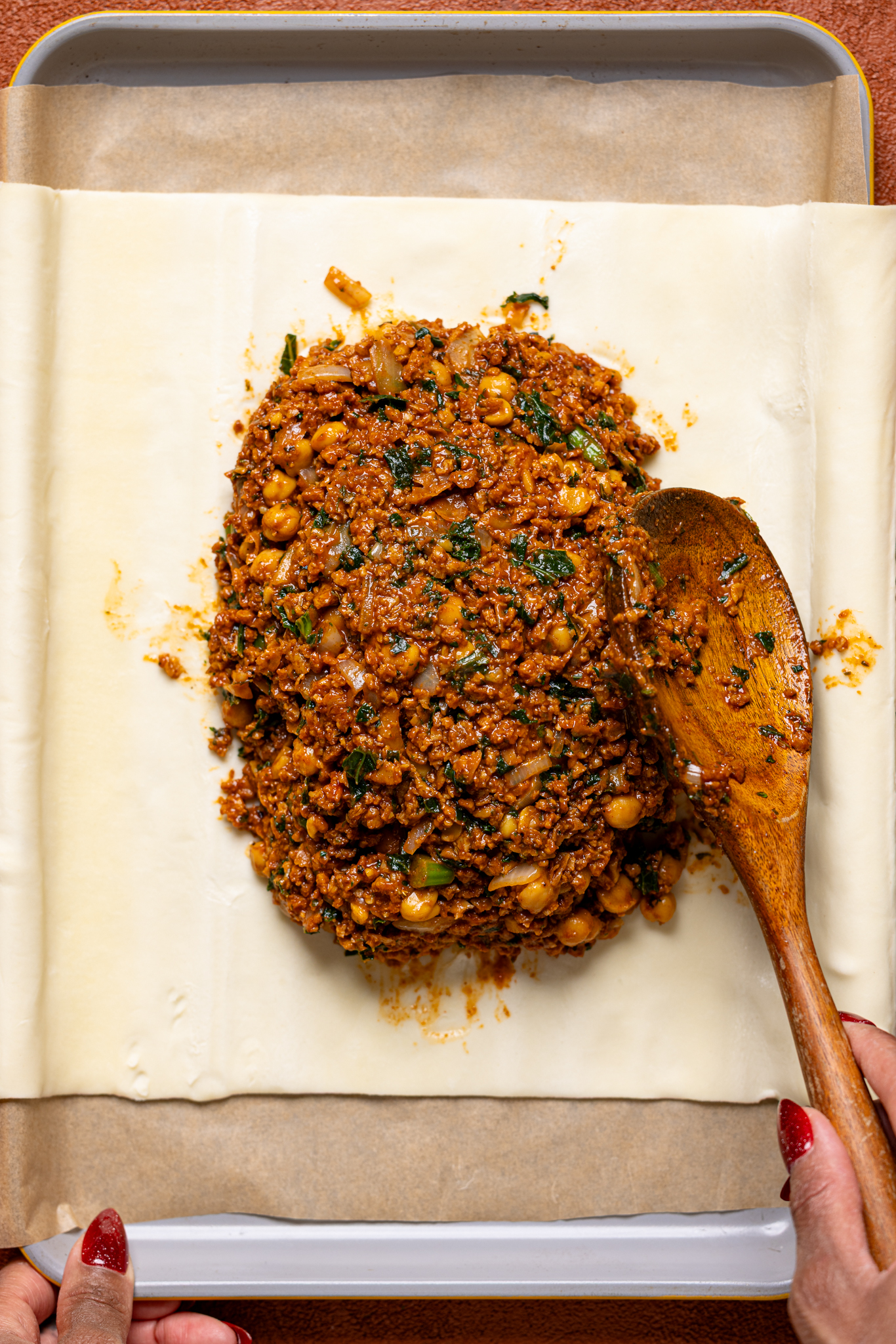 Image of beef Wellington filling being spooned onto the crust on a baking sheet with parchment.