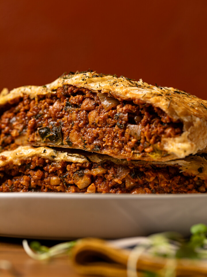 Up close shot of vegan beef Wellington sliced and stacked on each other on a plate.