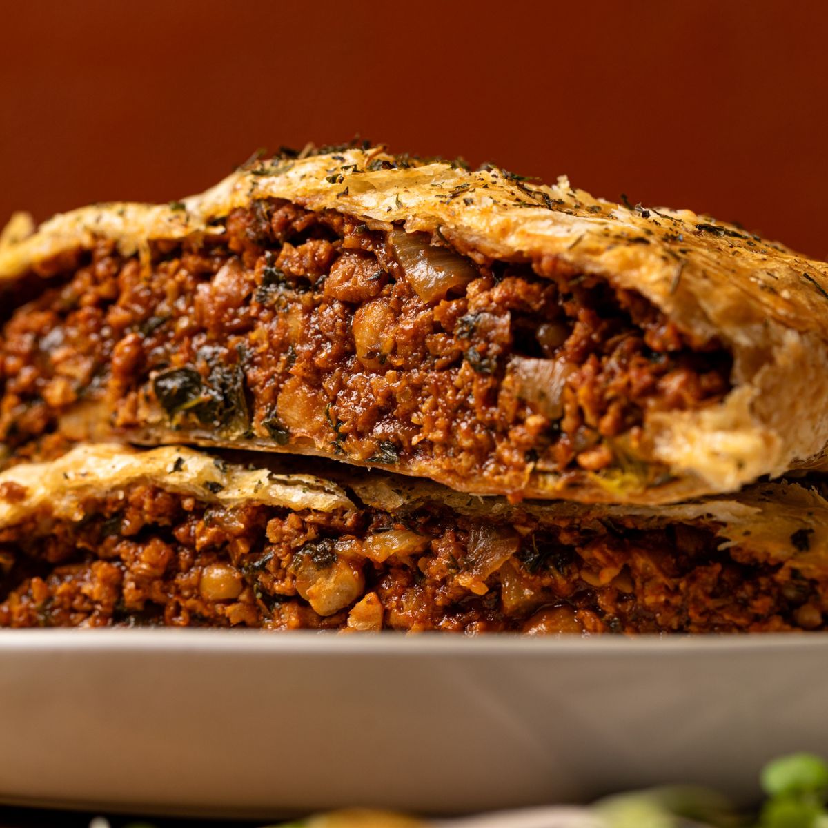 Up close shot of vegan beef Wellington sliced and stacked on each other on a plate.