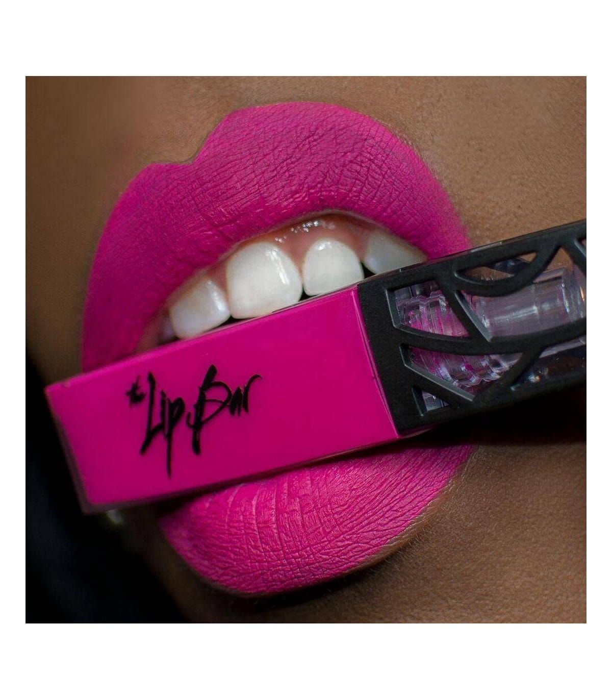 Mouth with bright pink lips biting down on a container of lipstick from the Lip Bar