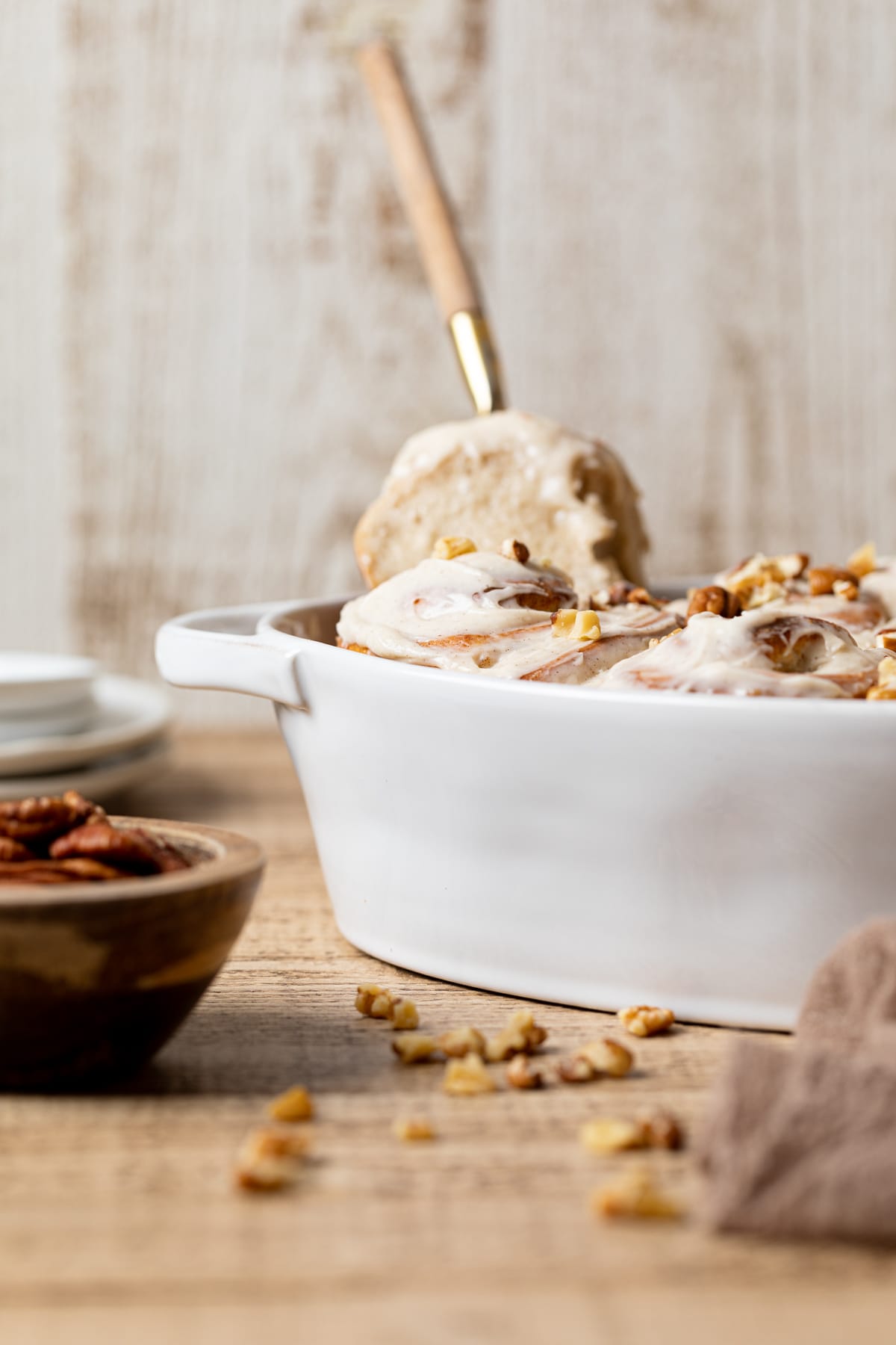 Fork grabbing a Banana Bread Cinnamon Roll with Maple Cream Cheese Frosting from a baking pan