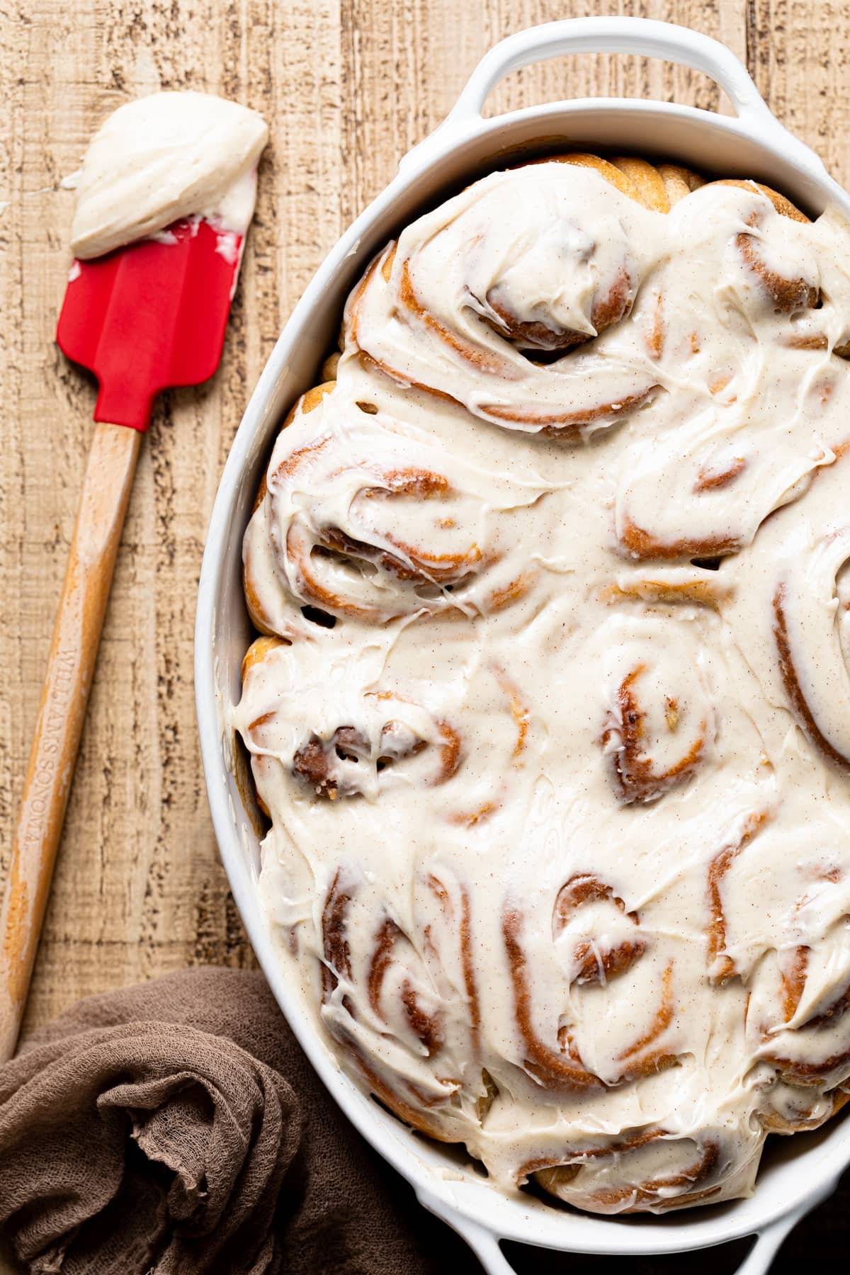 Spatula next to a baking pan of Banana Bread Cinnamon Rolls with Maple Cream Cheese Frosting 