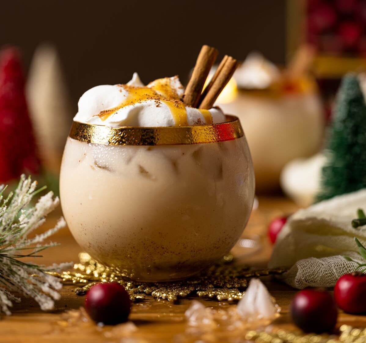 Vegan Caramel Eggnog Mocktail topped with coconut whipped cream, cinnamon sticks, and caramel sauce in a gold-rimmed glass