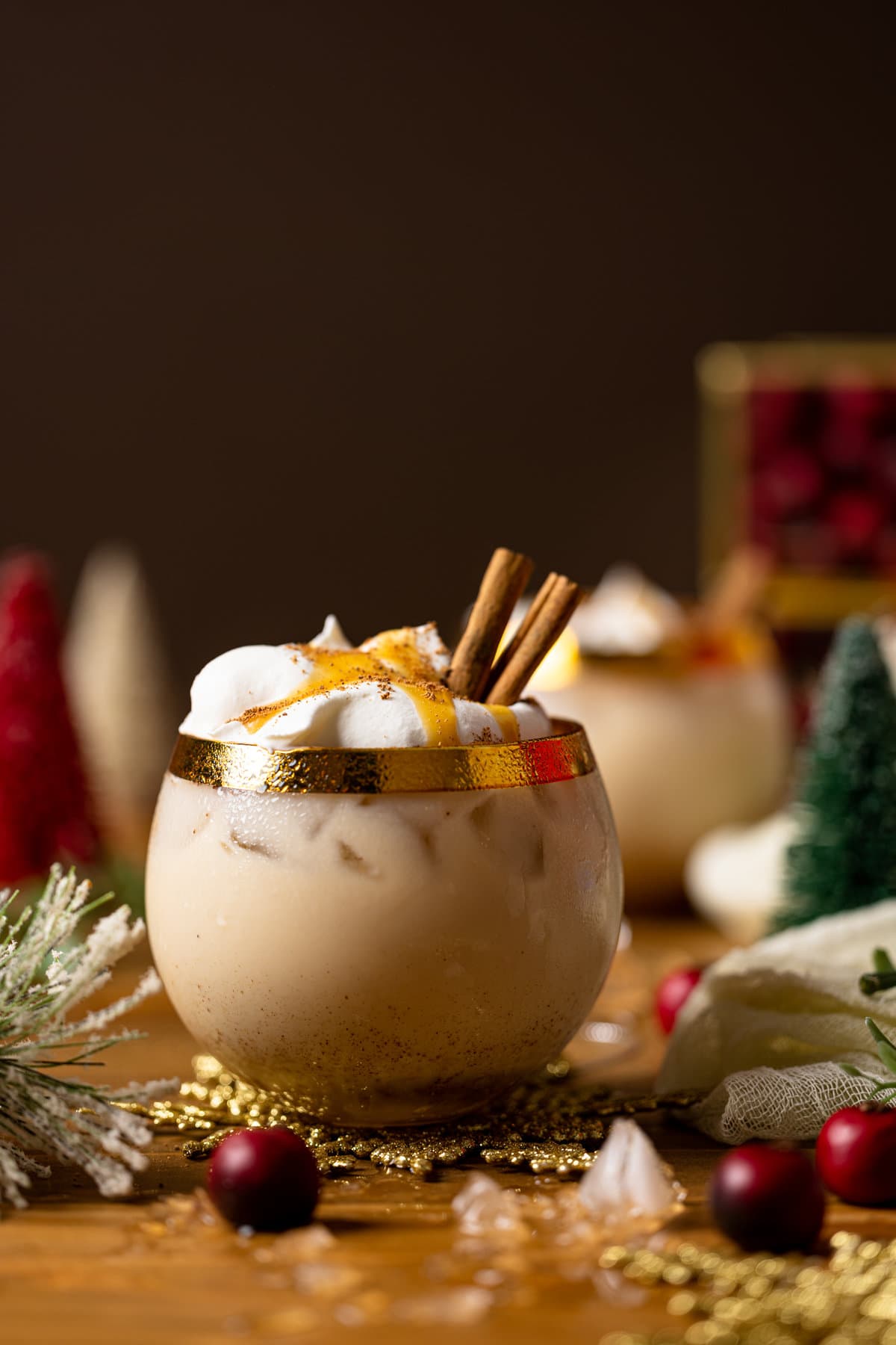 Vegan Caramel Eggnog Mocktail topped with coconut whipped cream, cinnamon sticks, and caramel sauce in a gold-rimmed glass
