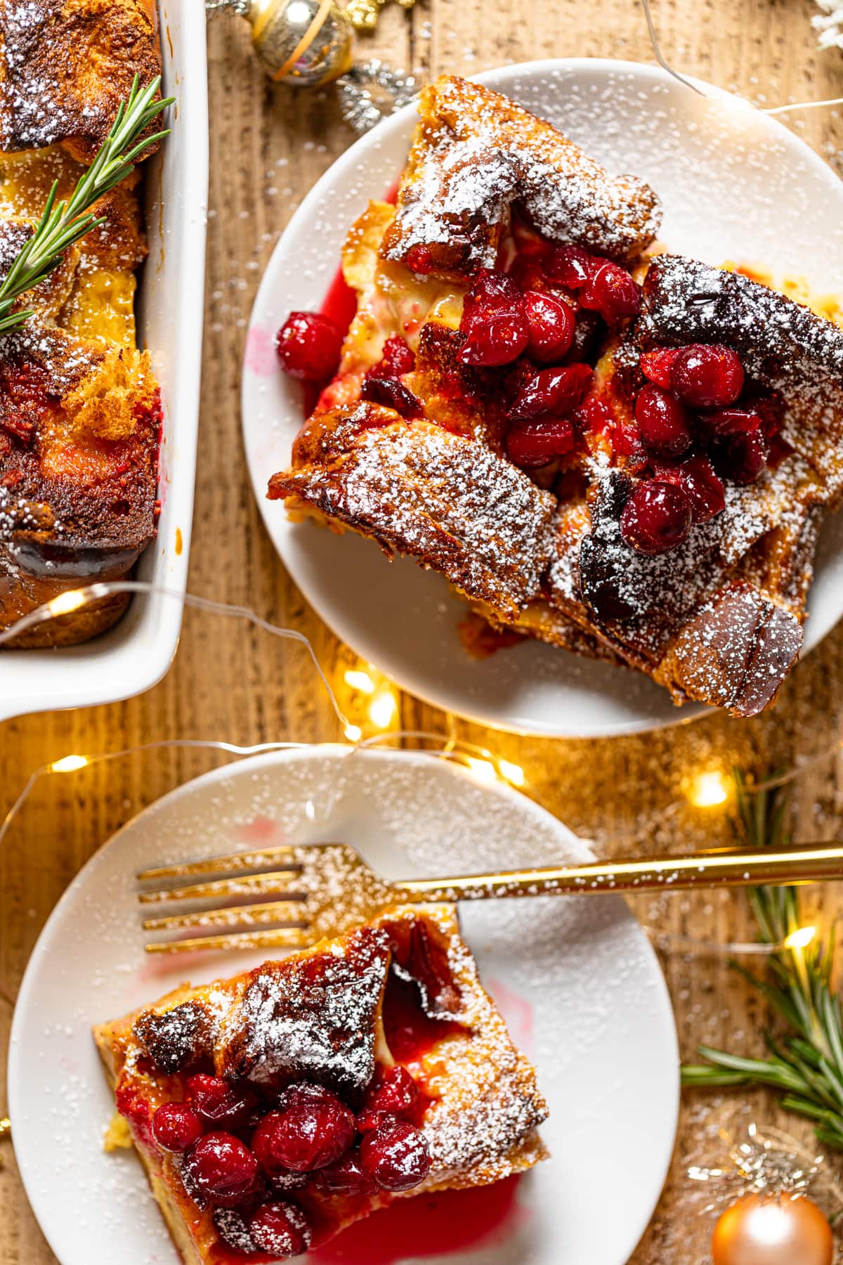 Pieces of Baked Eggnog French Toast on small plates sprinkled with powdered sugar