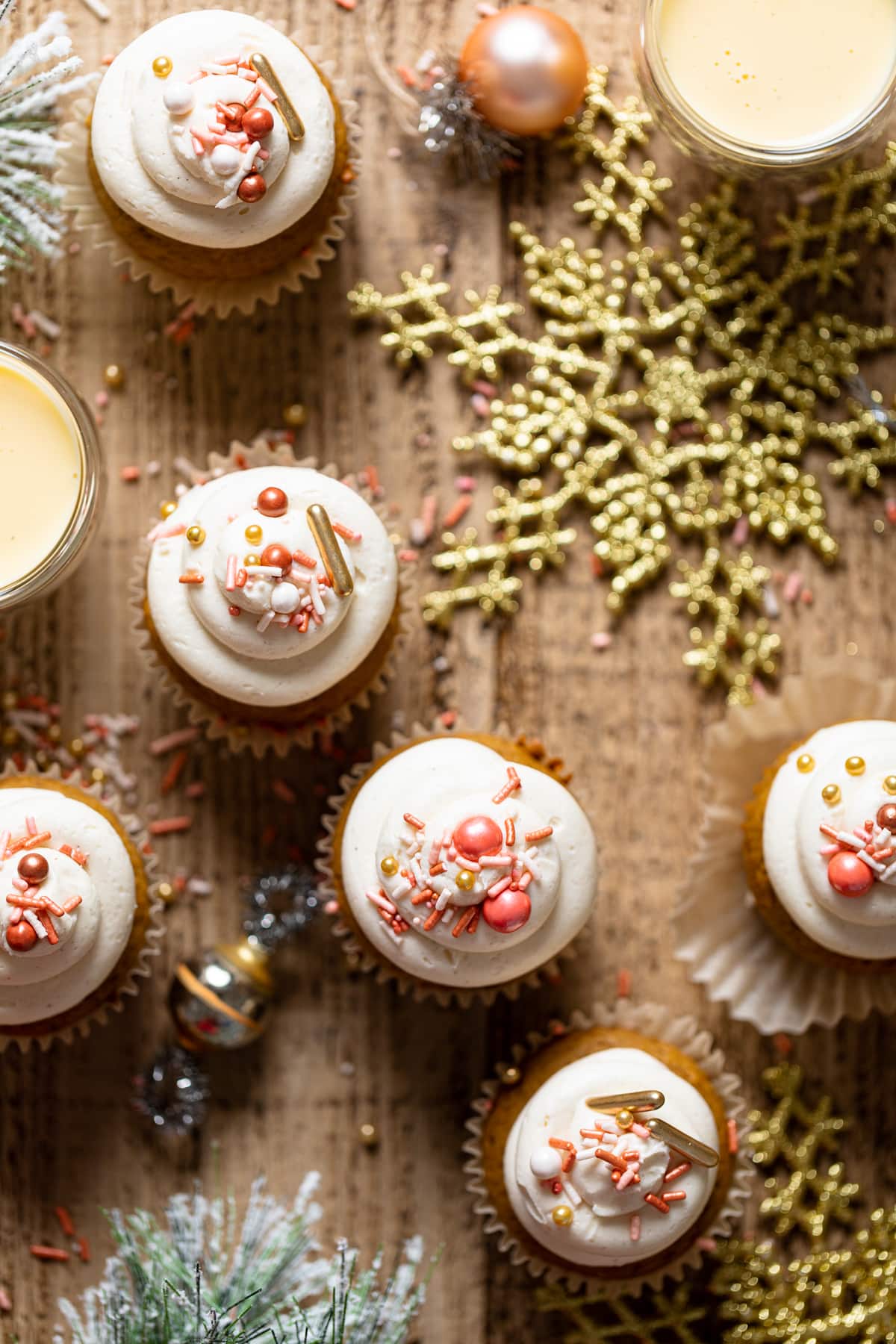 Gingerbread Cupcakes with Eggnog Frosting on a table with Christmas decorations including gold-colored snowflakes
